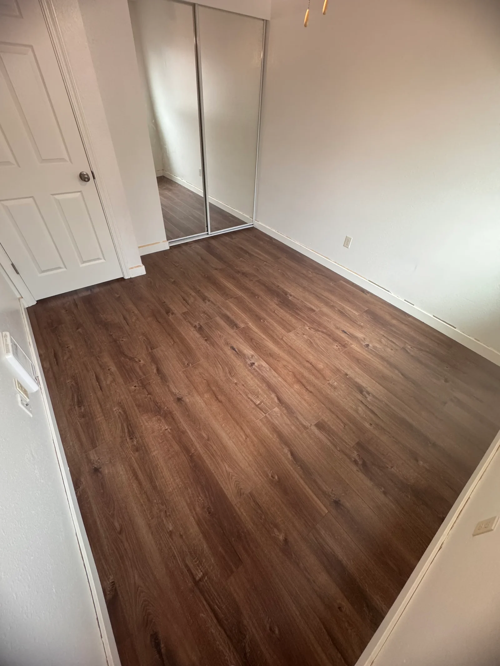 Brown vinyl plank flooring installed in bedroom with white trim and mirrored closet doors