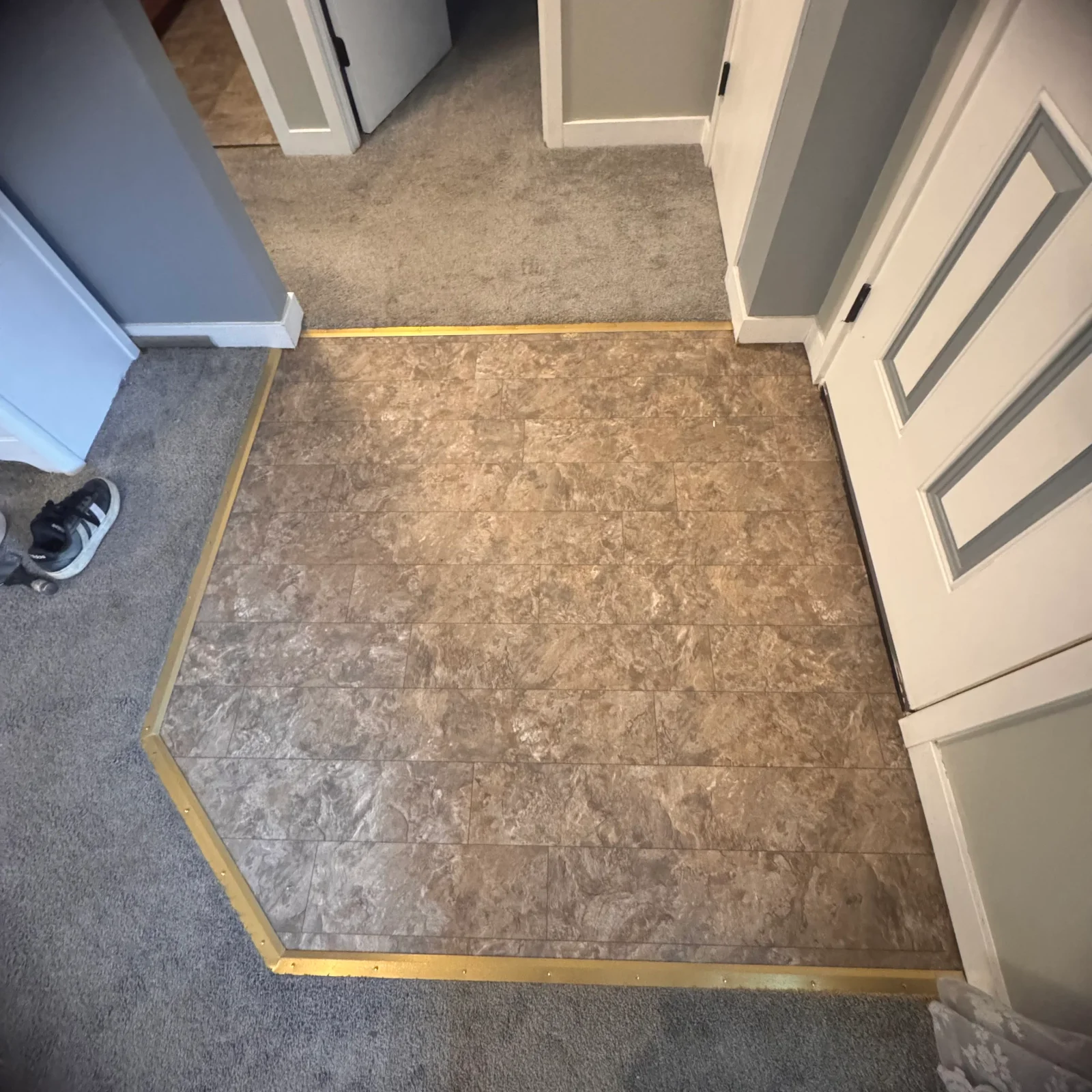 Stone-look ceramic tile flooring with brass transition trim between tile and carpet areas