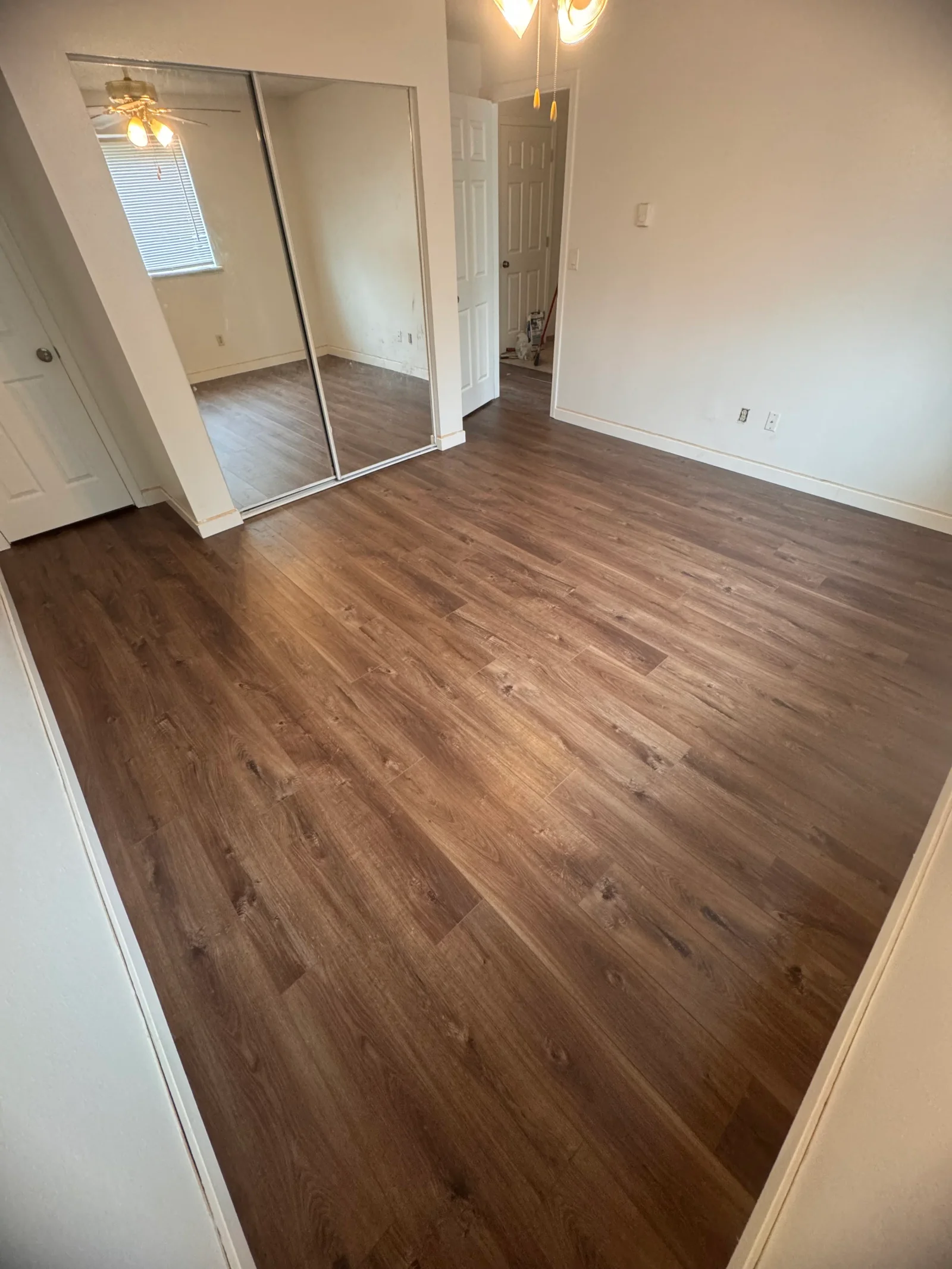 Brown luxury vinyl plank flooring installed in bedroom with mirrored closet doors and white walls