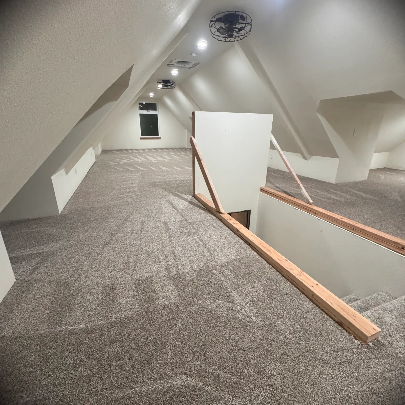 Gray textured carpet installed in attic with sloped ceilings, recessed lights, and wooden trim