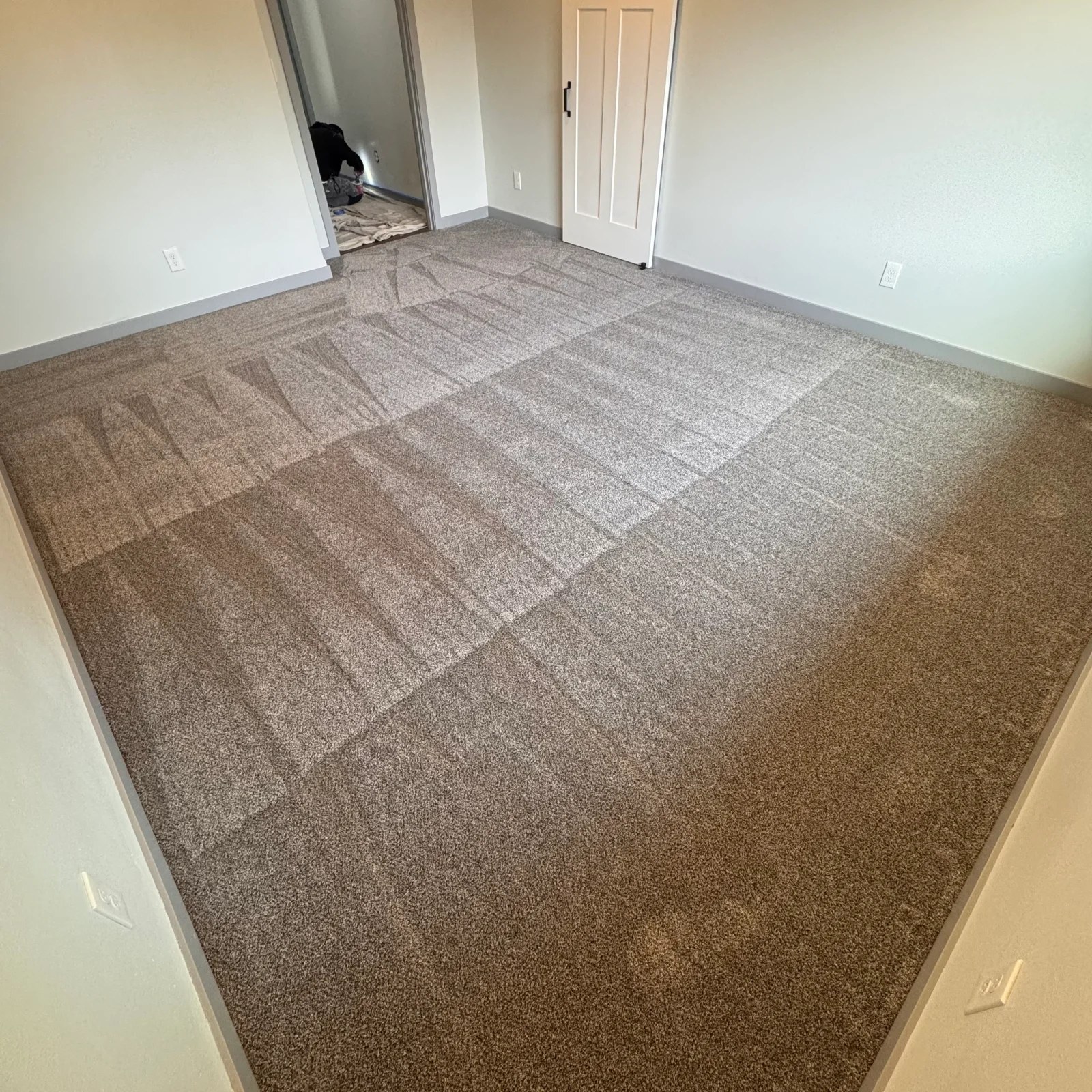 Installed carpet with visible seams in neutral tones, bedroom with white walls and closet doors
