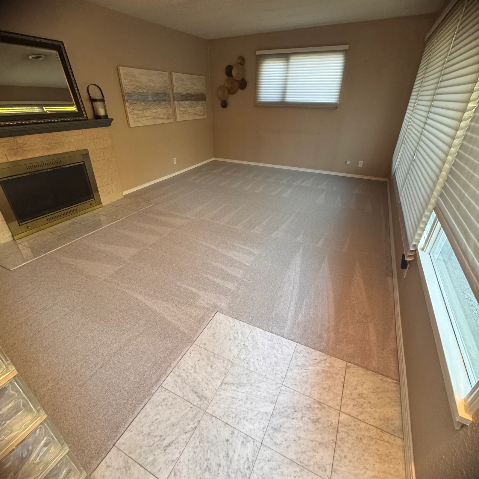 Neutral carpet installed in living room with marble tile transition and fireplace surround