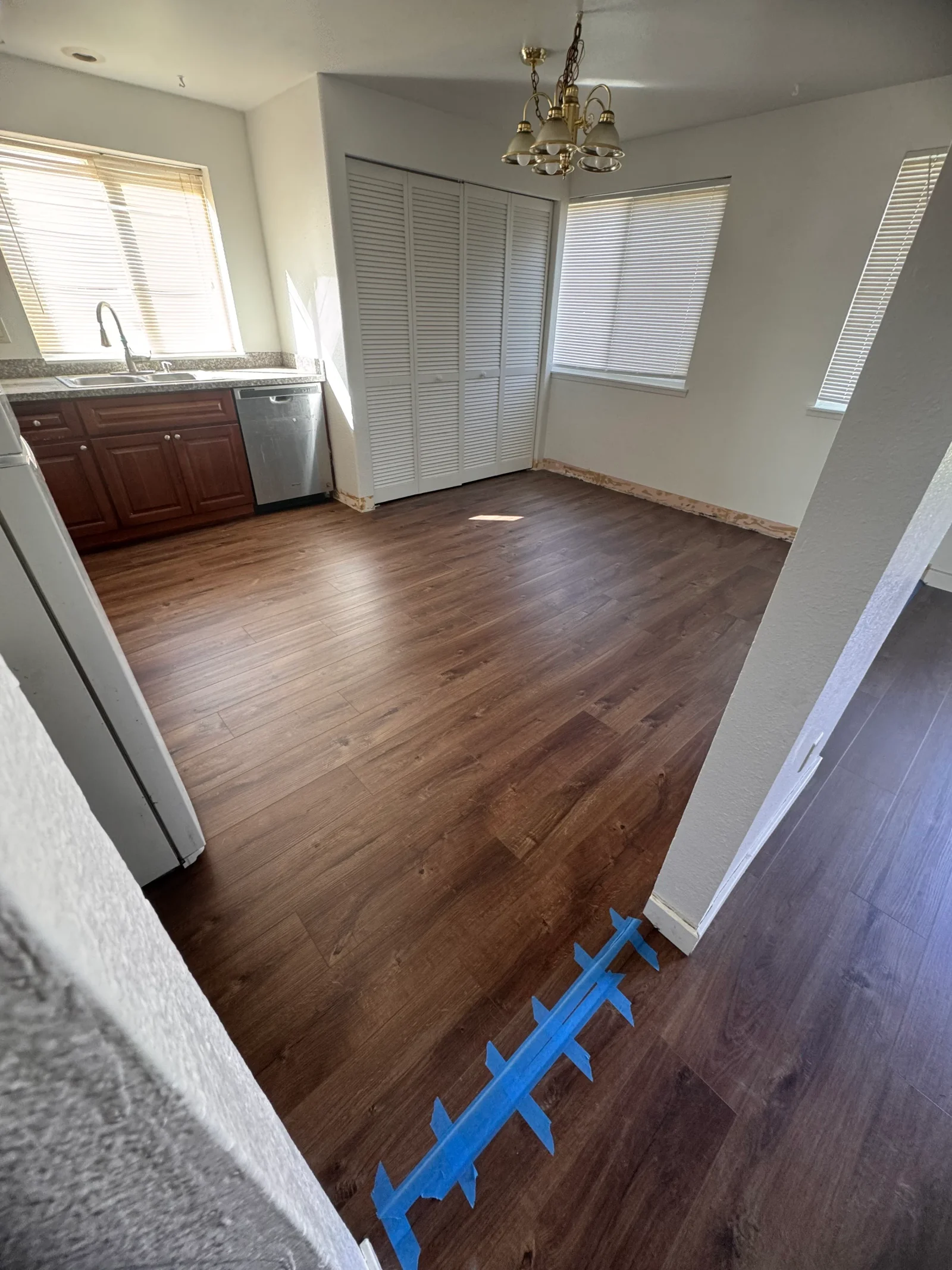 Medium-brown laminate flooring installed in kitchen and dining area with white walls and red cabinetry