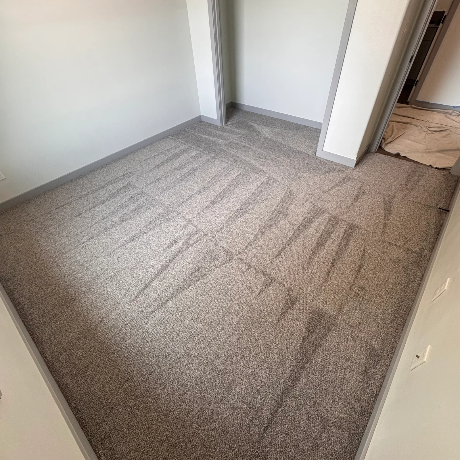 Neutral textured carpet installation with visible seams and white trim edging in interior room